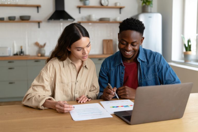Young multiracial couple reviewing finances on laptop in modern kitchen